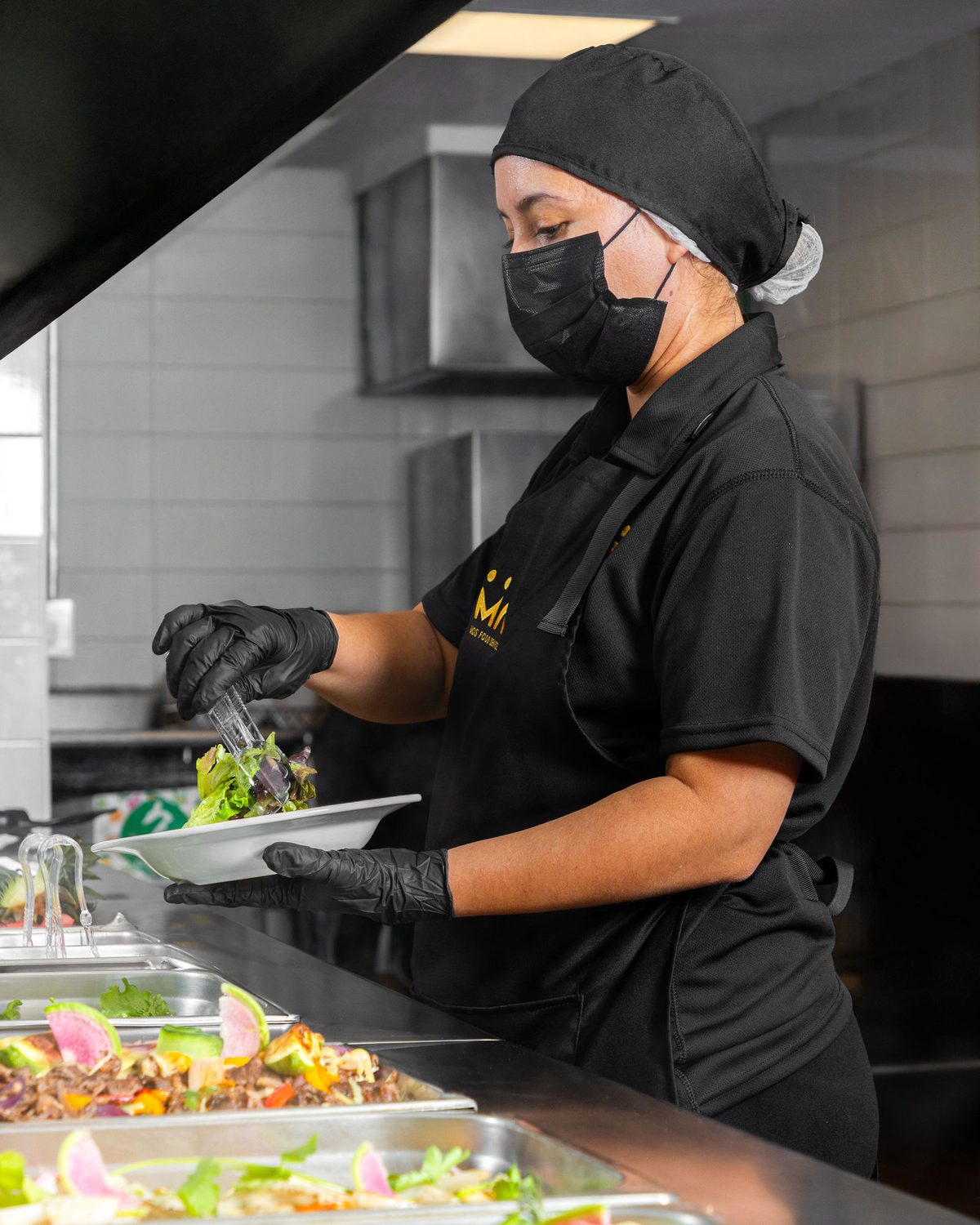 Personal de MOS Food Service con uniforme y cubrebocas sirviendo ensalada en la línea de servicio de un comedor industrial